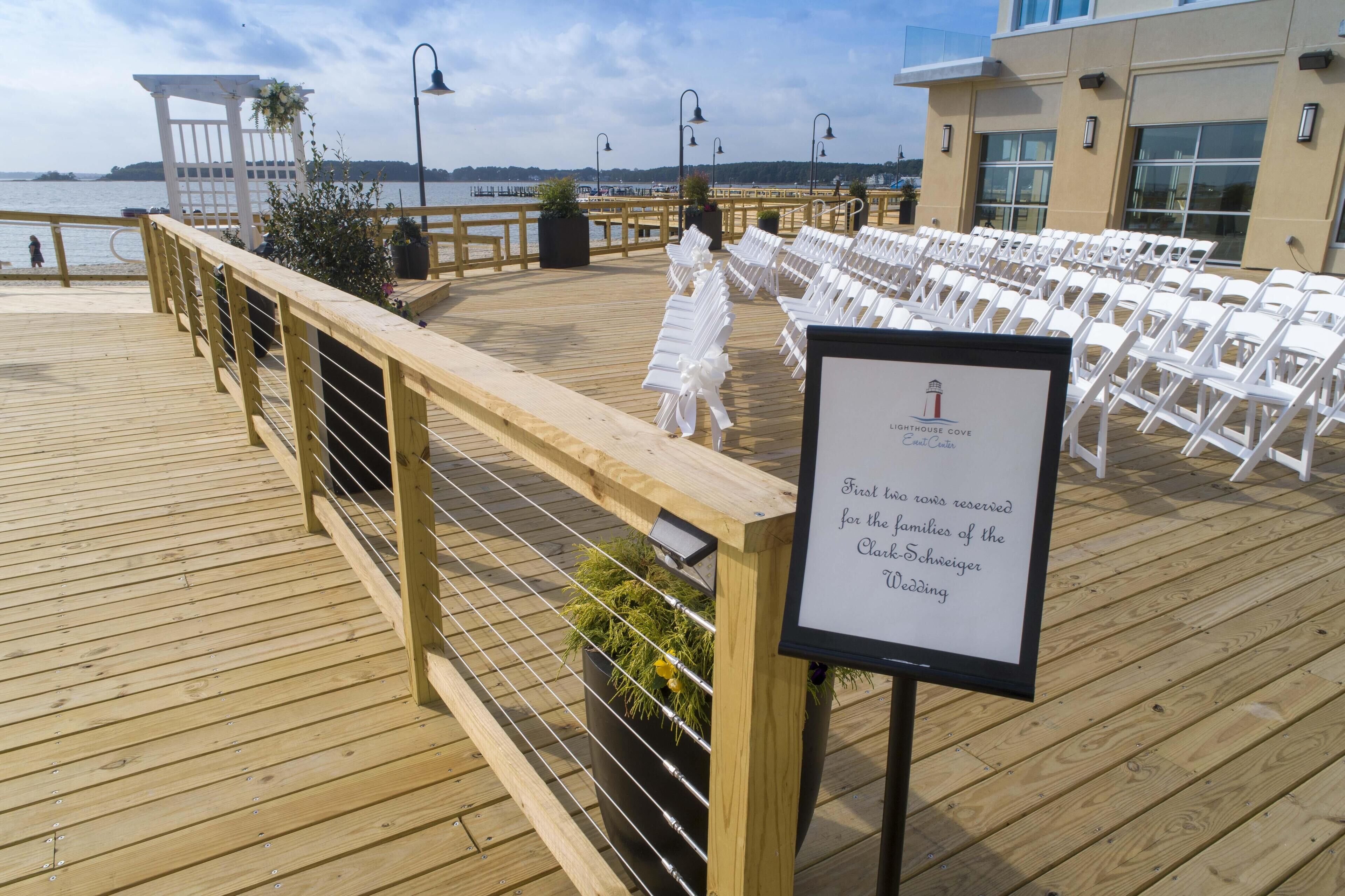 A wooden deck with white chairs arranged for an event, overlooking a body of water.