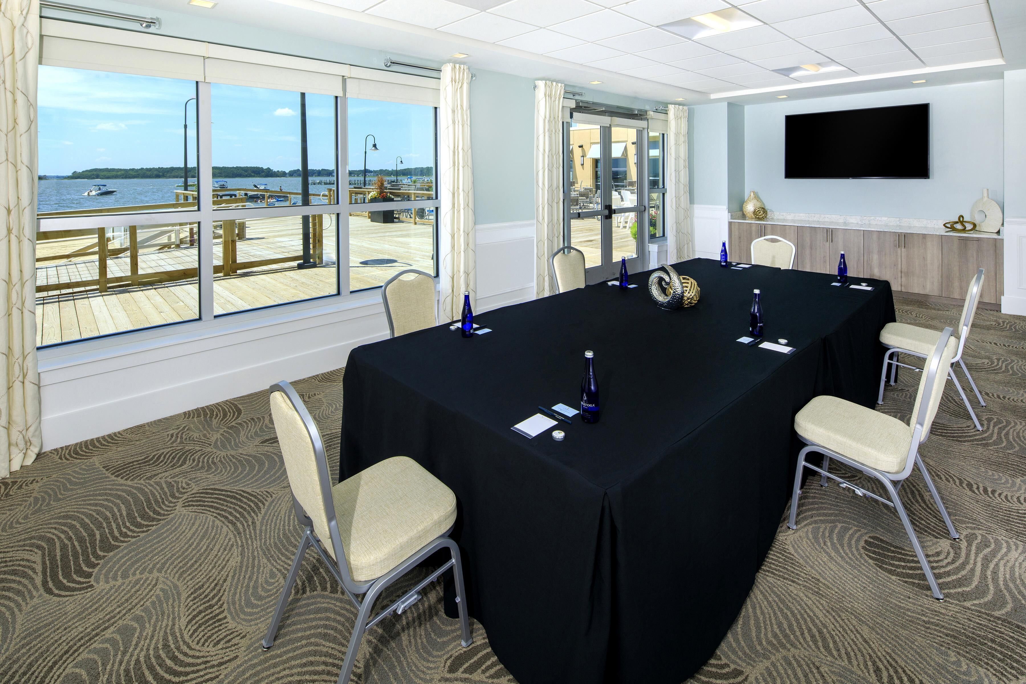 A conference room with a large table, chairs, a TV, and a view of the water.