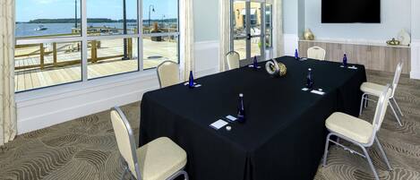 A conference room with a large table, chairs, a TV, and a view of the water.