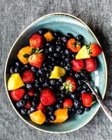 Un tazón con frutos rojos y trozos de piña sobre una superficie con textura.