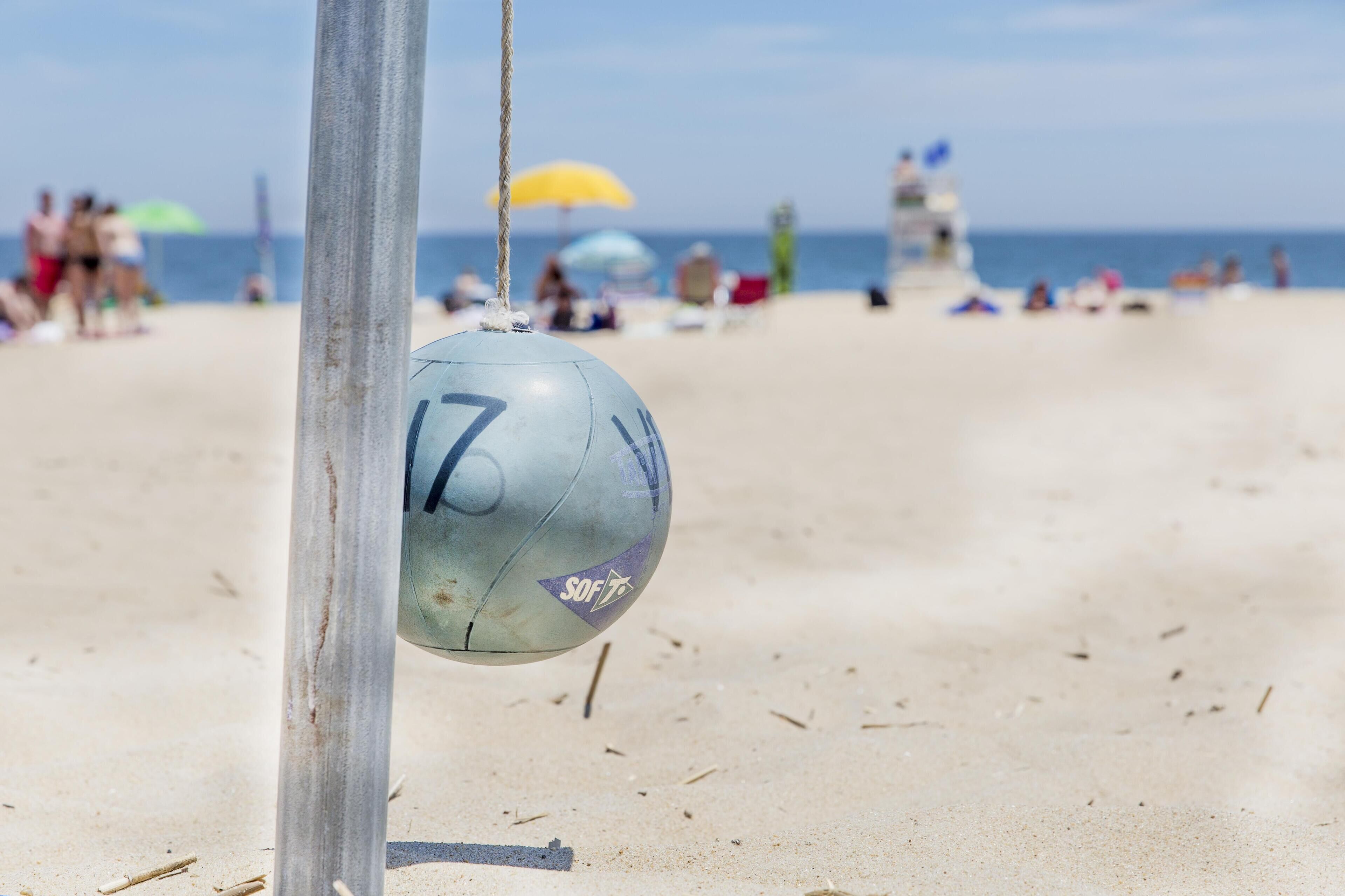 A beach volleyball with the number 17 and the word "SOFT" on a sandy beach with people in the background.
