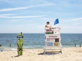 A lifeguard tower with names DEWEY and DICKINSON on it, a blue flag, and a green surfboard leaning against it.