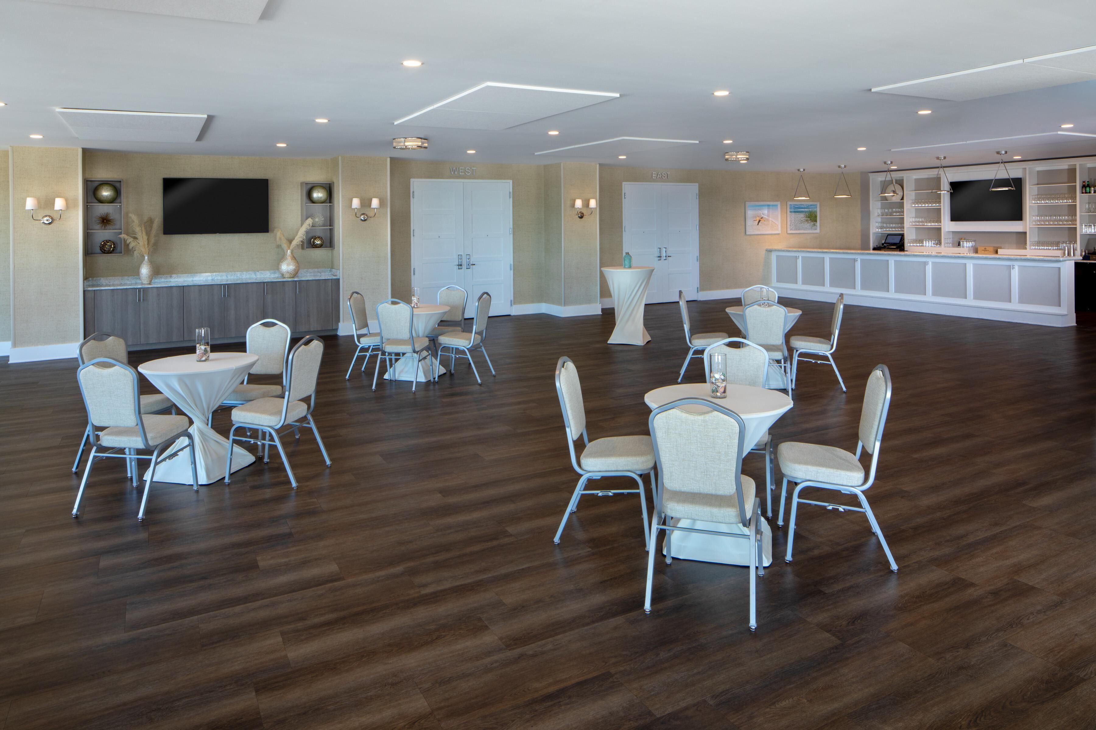 A spacious hotel lobby with multiple seating areas, a central bar, and a large flat-screen TV mounted on the wall.