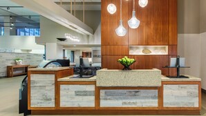 A reception desk with a wooden panel backdrop and a central island with a fruit bowl. - Hyatt Place Dewey Beach (Dewey Beach)