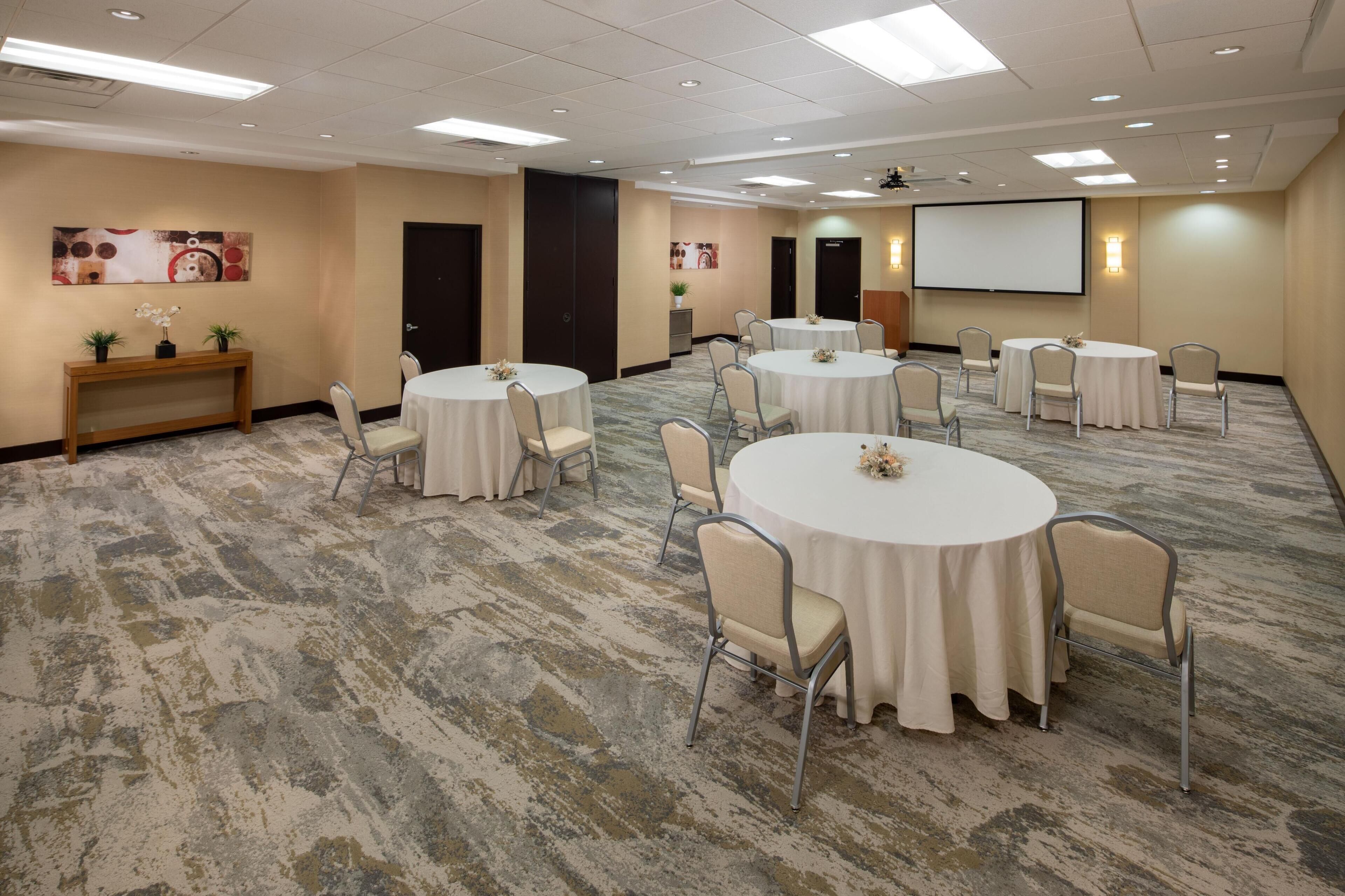 A conference room with round tables, chairs, a projector screen, and a carpeted floor.
