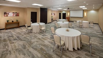 A conference room with round tables, chairs, a projector screen, and a carpeted floor.