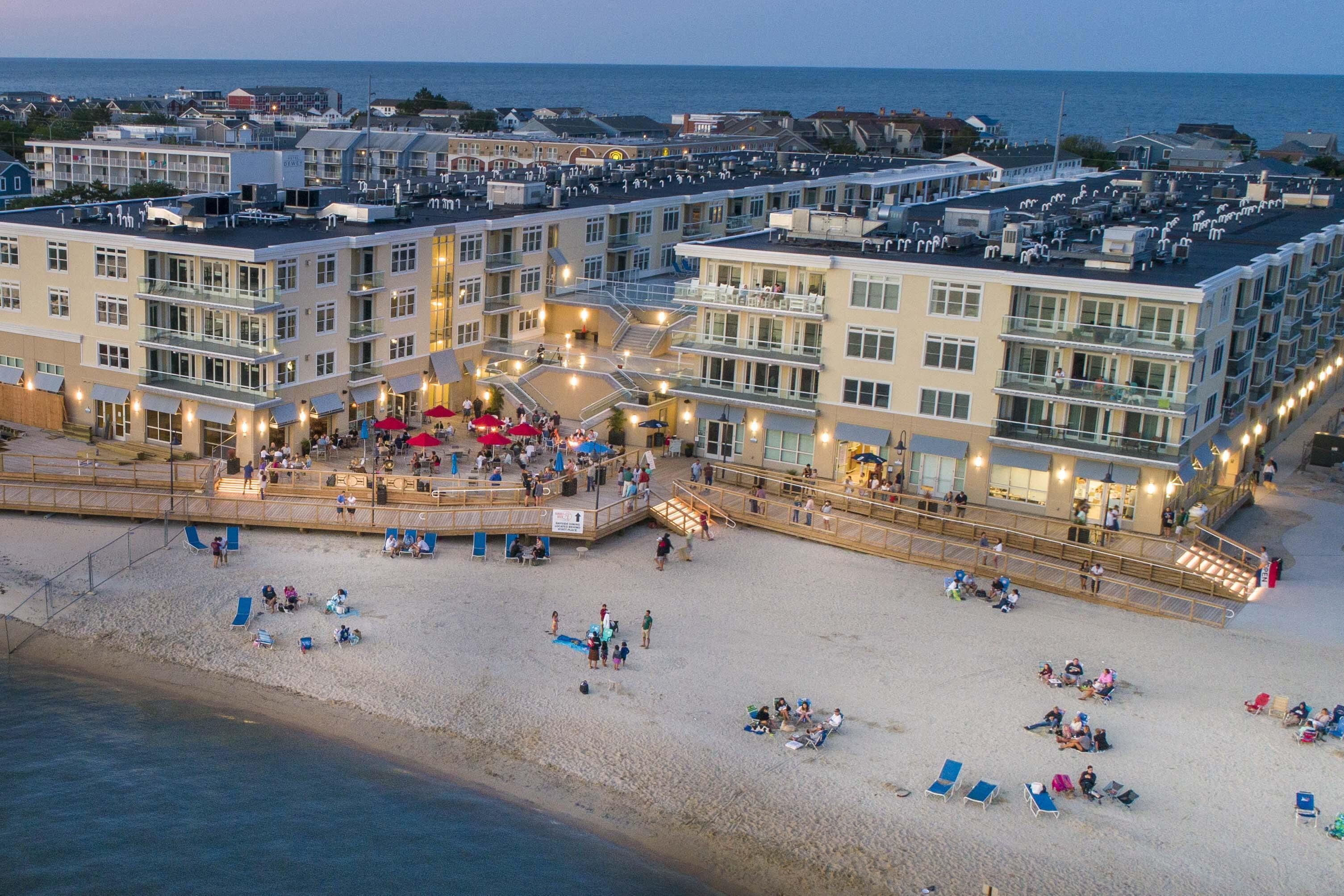 A beachfront hotel with multiple balconies, a boardwalk, and beach chairs.