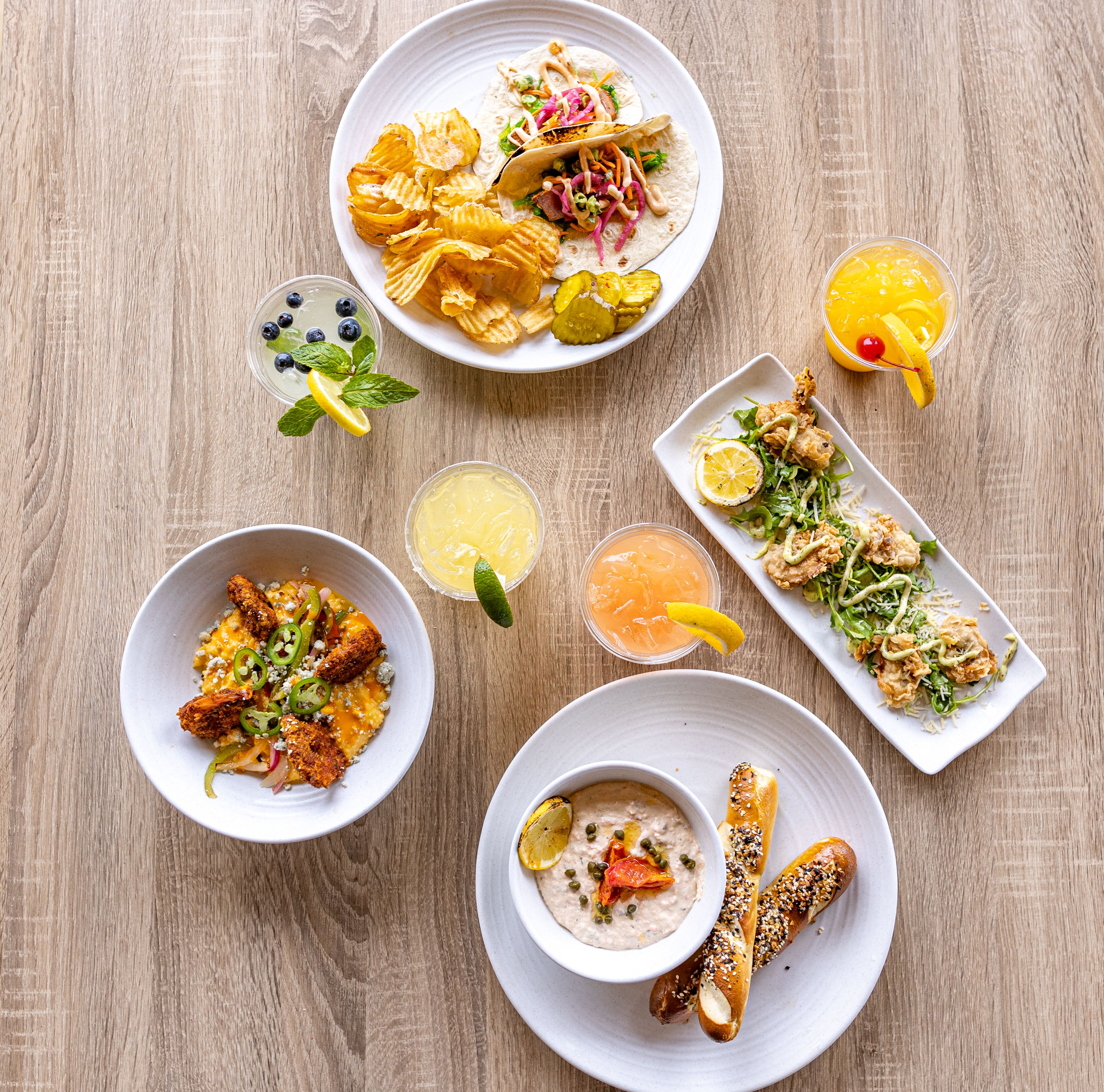 A variety of dishes including tacos, a salad, and breadsticks, arranged on a wooden table.
