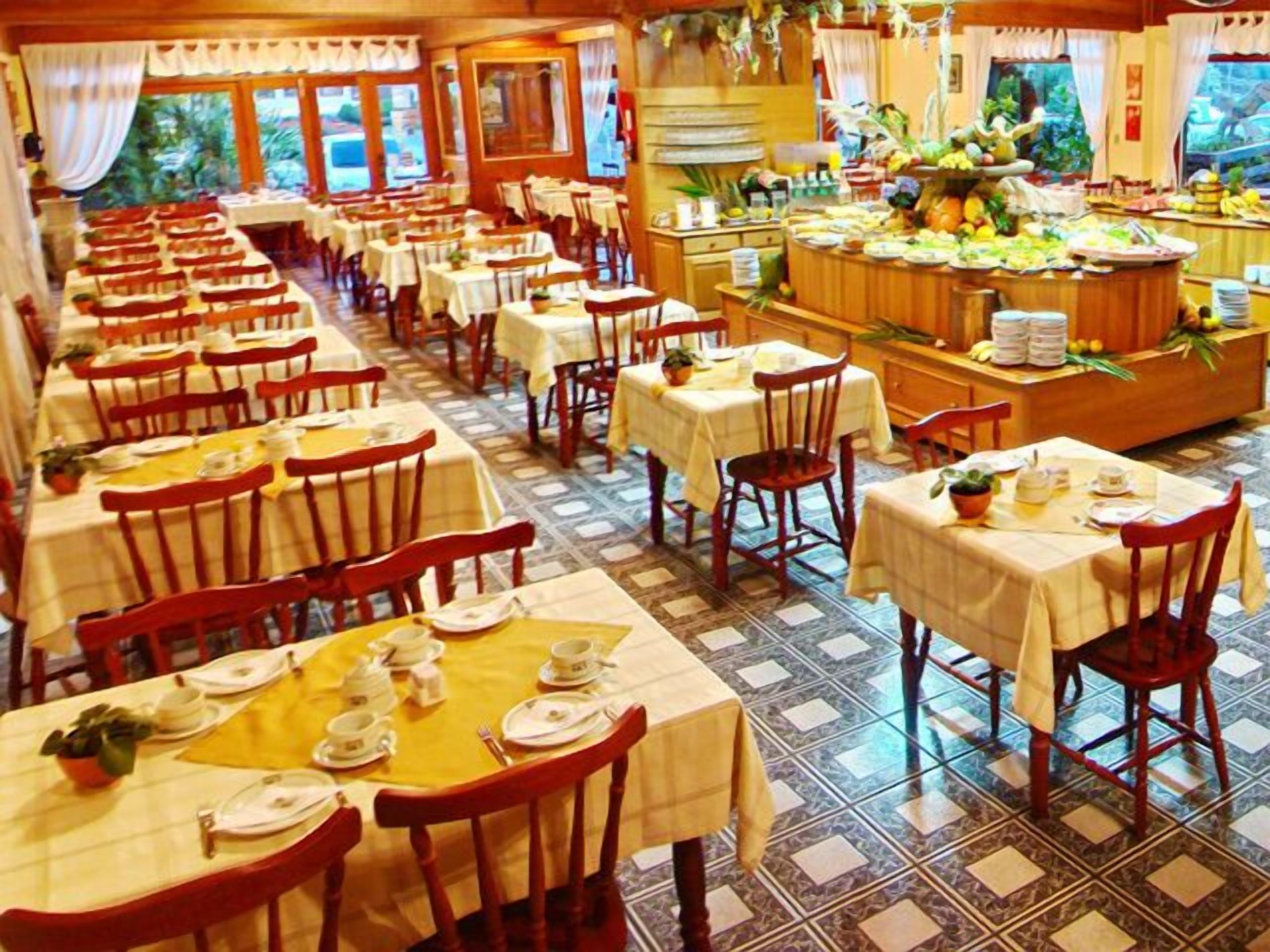 A restaurant with multiple tables and chairs, a buffet area with various food items, and a tiled floor.