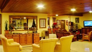 Un salon avec des fauteuils jaunes, des meubles en bois, un téléviseur et un plafond en bois.