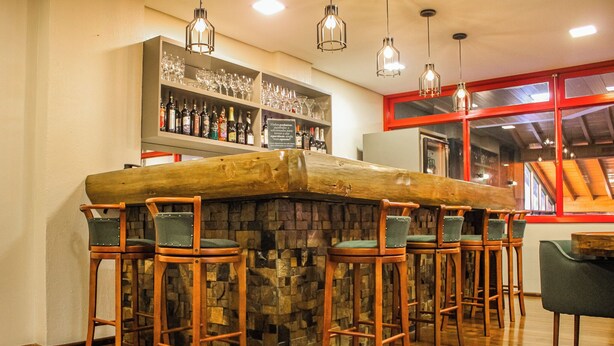 A bar area with a stone counter, multiple stools, and a wine and liquor display. - Hotel Fioreze Origem (Gramado)