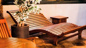 A wooden lounge chair with a potted plant, a small wooden stool, and a tiled floor. - Hotel Fioreze Origem (Gramado)