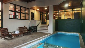 An indoor swimming pool with a tiled edge, wooden lounge chairs, and a staircase leading to an upper level. - Hotel Fioreze Origem (Gramado)