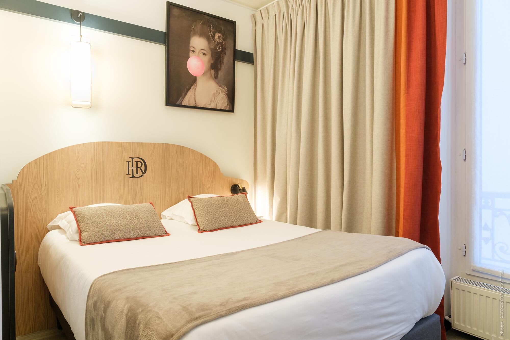 Ein Hotelzimmer mit hölzernem Kopfteil, zwei gemusterten Kissen, einer beigen Decke und einem Bild an der Wand.