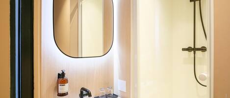 A bathroom with a white sink, a mirror, a shower, and a bottle of soap.