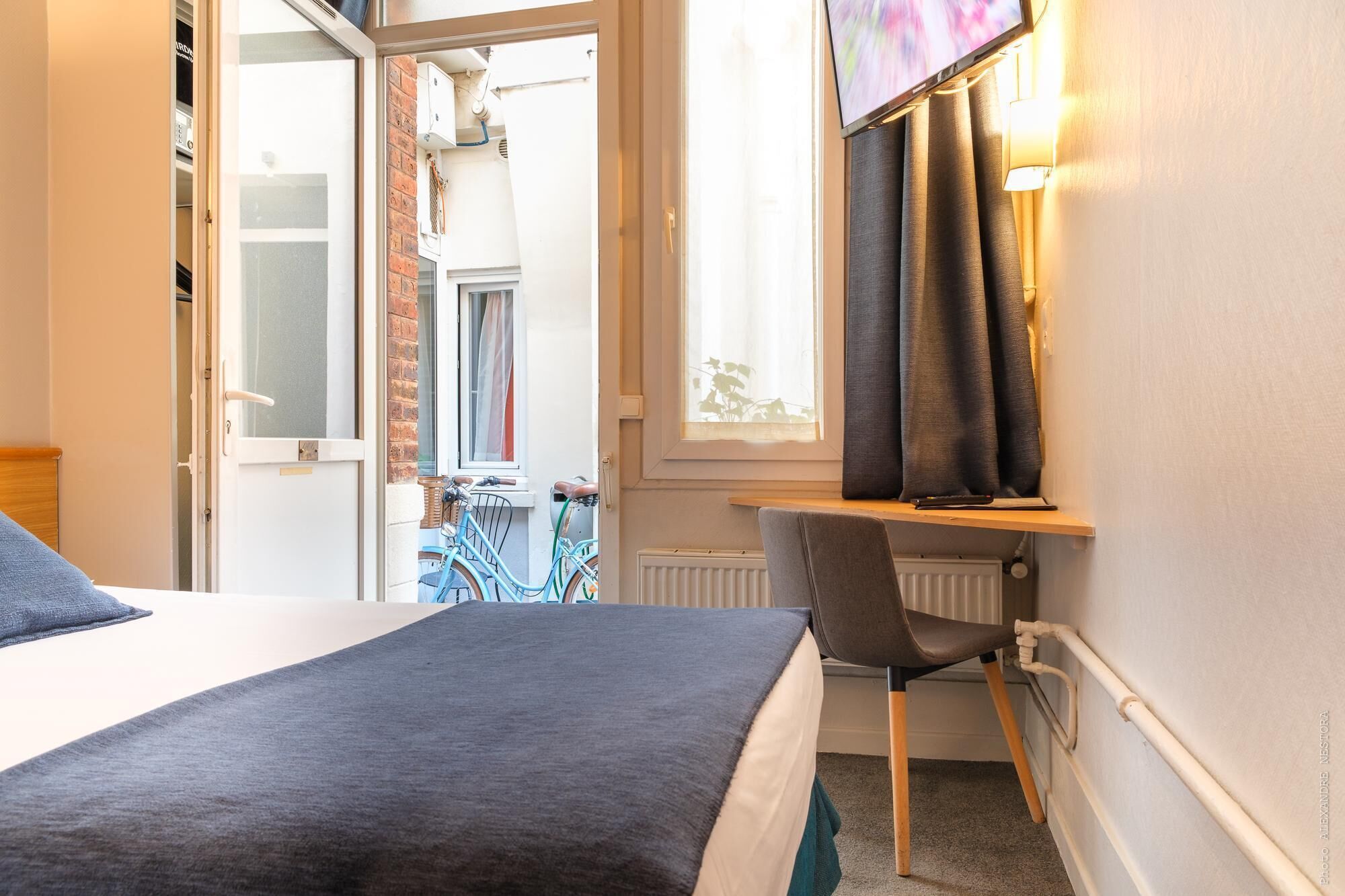 Une chambre à coucher avec un lit, une chaise, une fenêtre avec des rideaux et un vélo à l’extérieur.