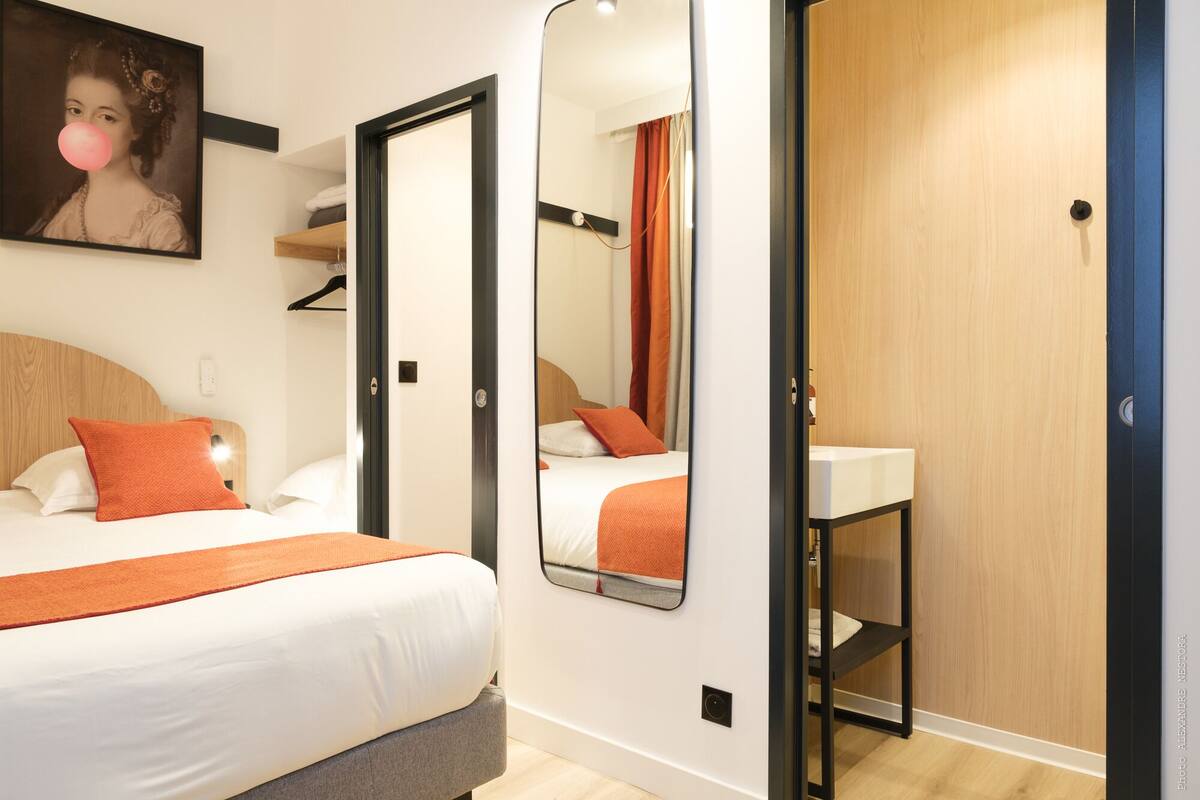 Quarto de hotel com duas camas, um espelho, um guarda-roupa e uma pequena prateleira.
