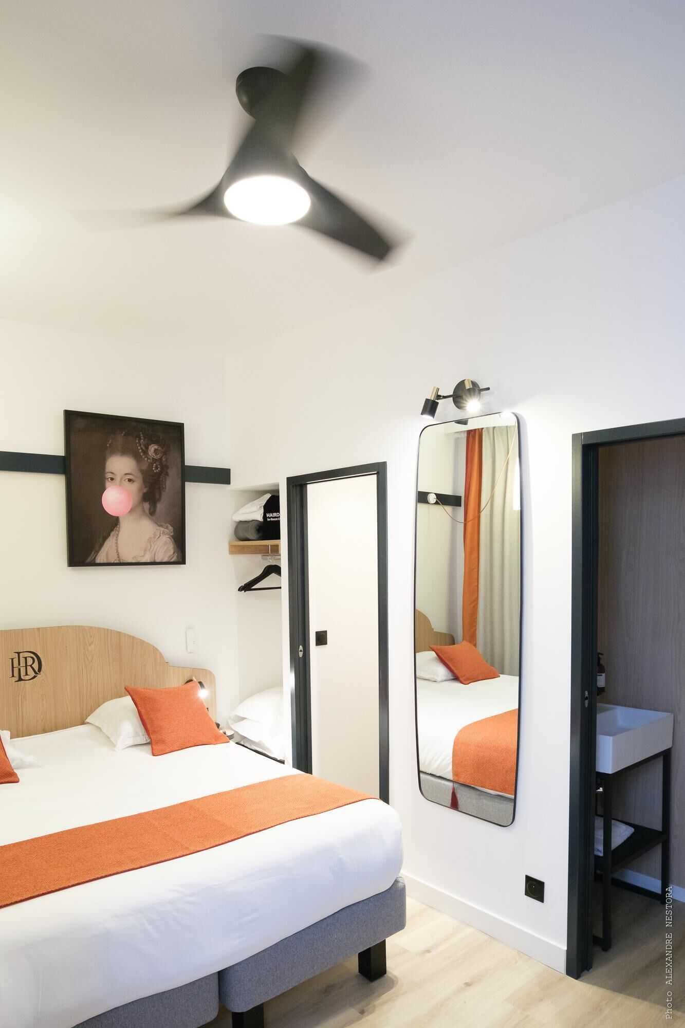 A modern hotel room with a bed, a mirror, a wardrobe, and a ceiling fan.