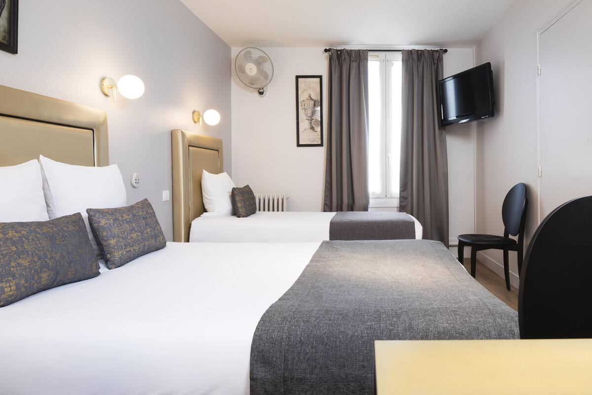 Quarto de hotel com duas camas, televisão, uma cadeira e janela com cortinas.