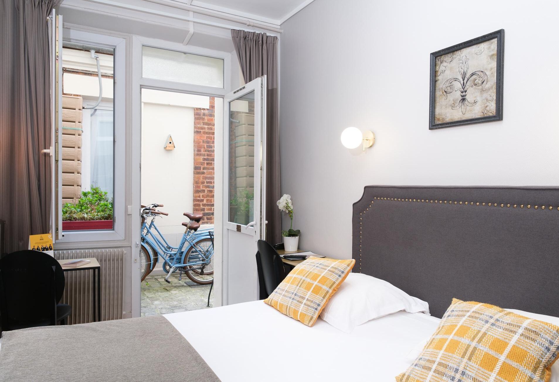 Habitación de hotel con cama, una silla, una mesa, una bicicleta y vista al exterior.