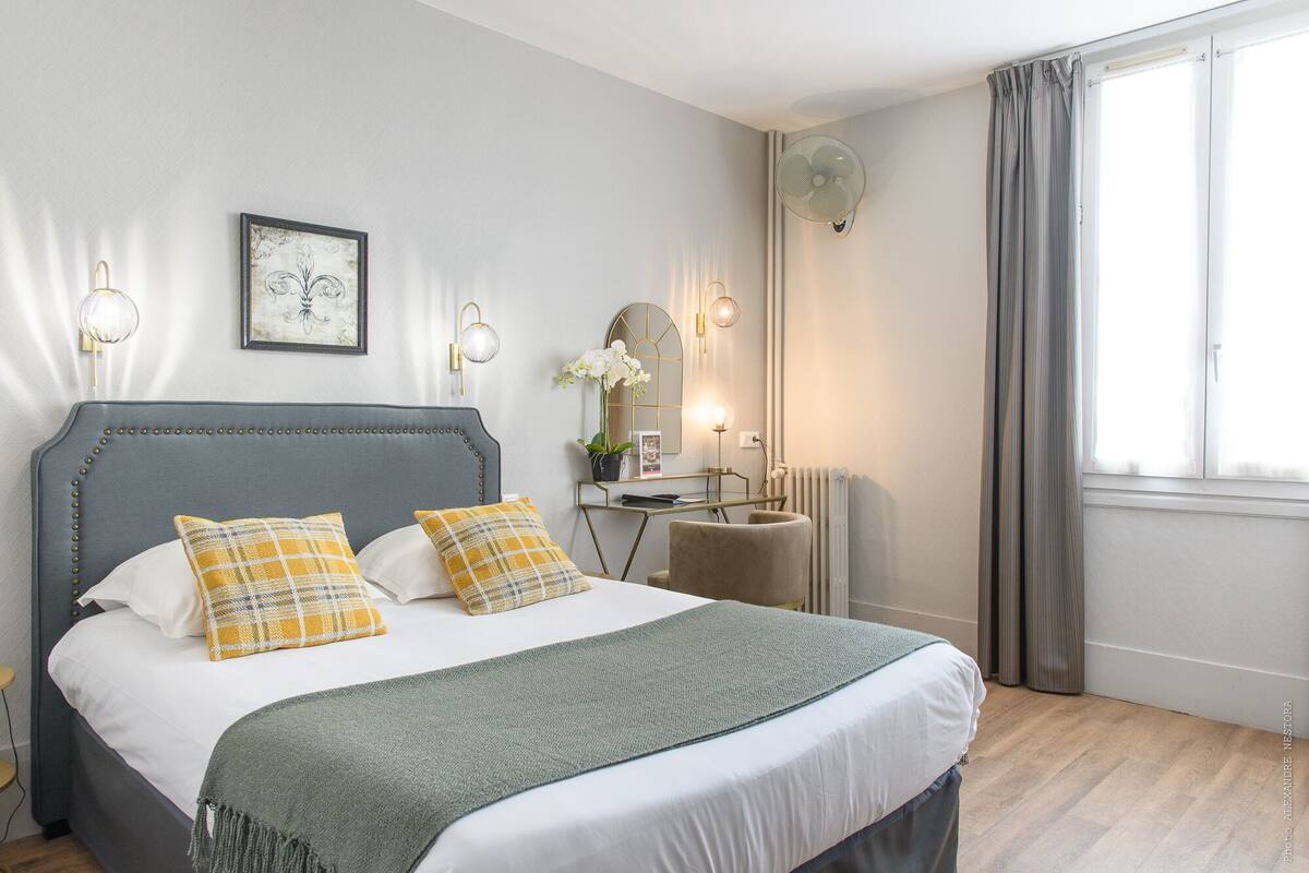 Quarto bem arrumado com uma cama, mesas de cabeceira, um espelho e uma janela com cortinas.