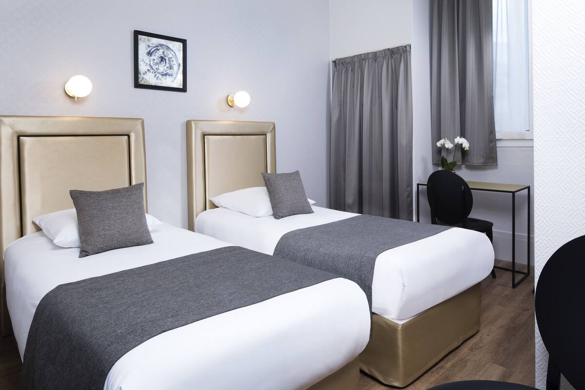 Quarto de hotel com duas camas, uma escrivaninha e uma cadeira.