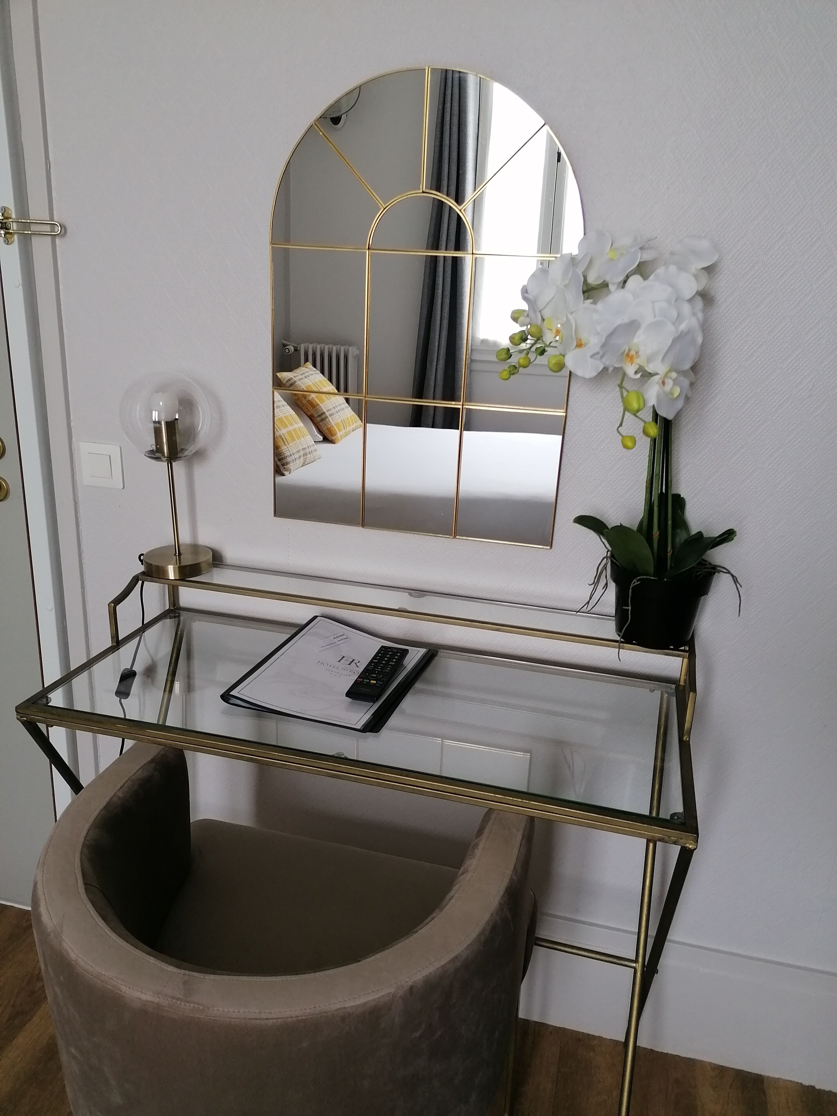Une salle de bain moderne avec un meuble-lavabo en verre, un lavabo rond, un miroir avec un cadre doré et une orchidée en pot.