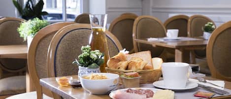 Una mesa para dos dispuesta para el desayuno, con cruasanes, un tazón de cereal, un plato de jamón y una taza de café.