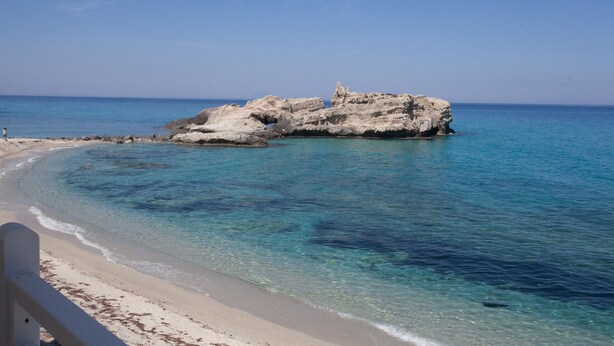 A beach with clear turquoise water, a rocky outcrop, and a sandy shore.
