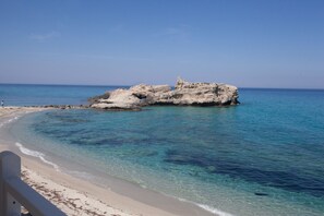 Una playa con agua turquesa cristalina, un promontorio rocoso y una orilla arenosa.