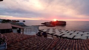 A coastal view with a sunset, a rocky outcrop, and a tiled terrace.
