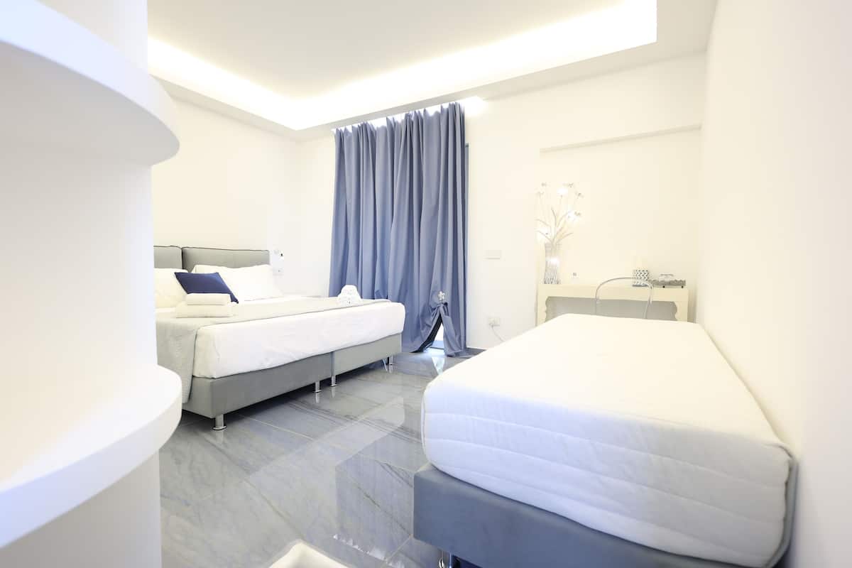 A modern hotel room with two beds, a large window with curtains, a bedside table, and a small bathroom area.