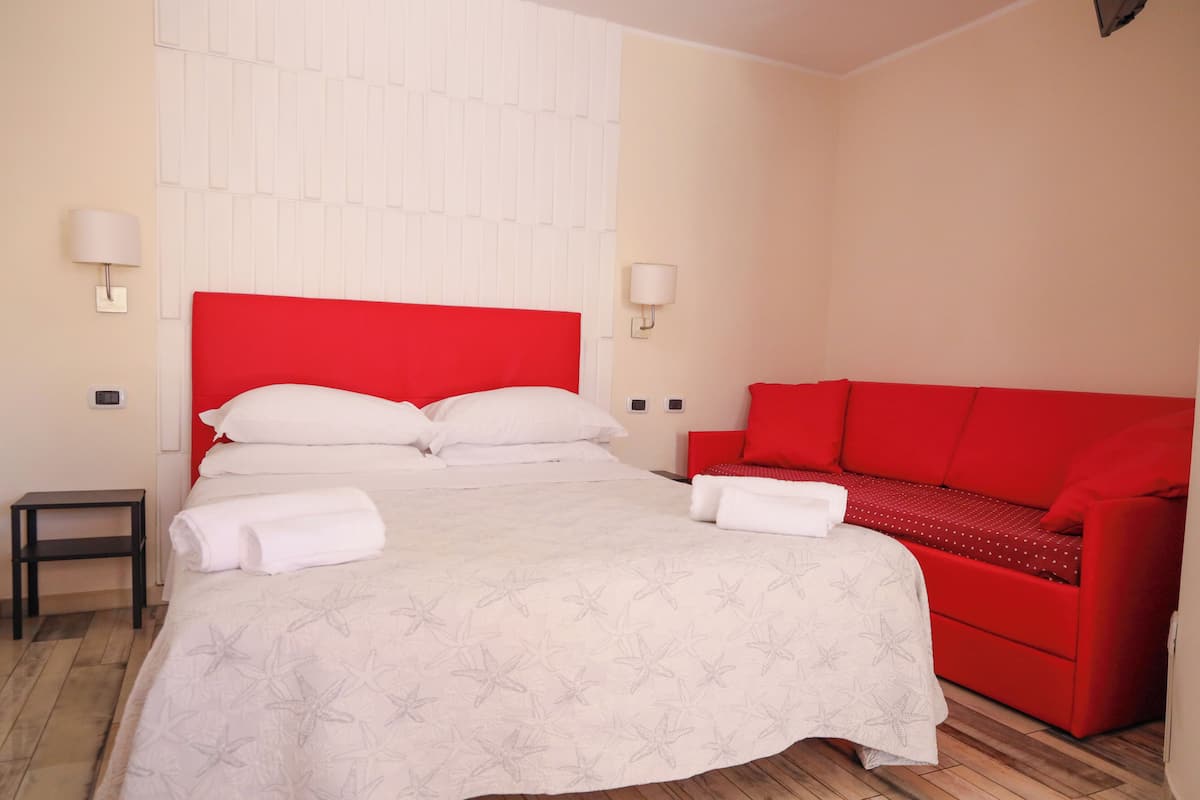 A hotel room with a bed, a red sofa, and two wall-mounted lamps.
