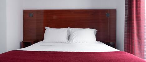 A neatly made bed with a wooden headboard, white bedding, and a red blanket.