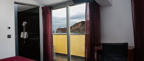 A hotel room with a bed, a chair, a sliding glass door leading to a balcony, and a TV mounted on the wall.