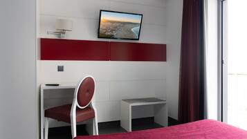 A modern hotel room with a bed, a desk with a chair, a television mounted on the wall, and a window with curtains.