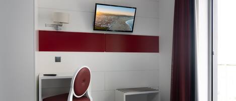 Une chambre d’hôtel moderne équipée d’un lit, d’un bureau avec une chaise, d’un téléviseur fixé au mur et d’une fenêtre avec des rideaux.
