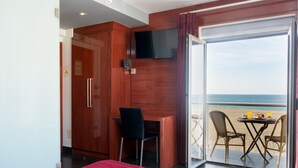 A hotel room with a bed, a desk, a chair, a TV, and a balcony with a table and chairs.