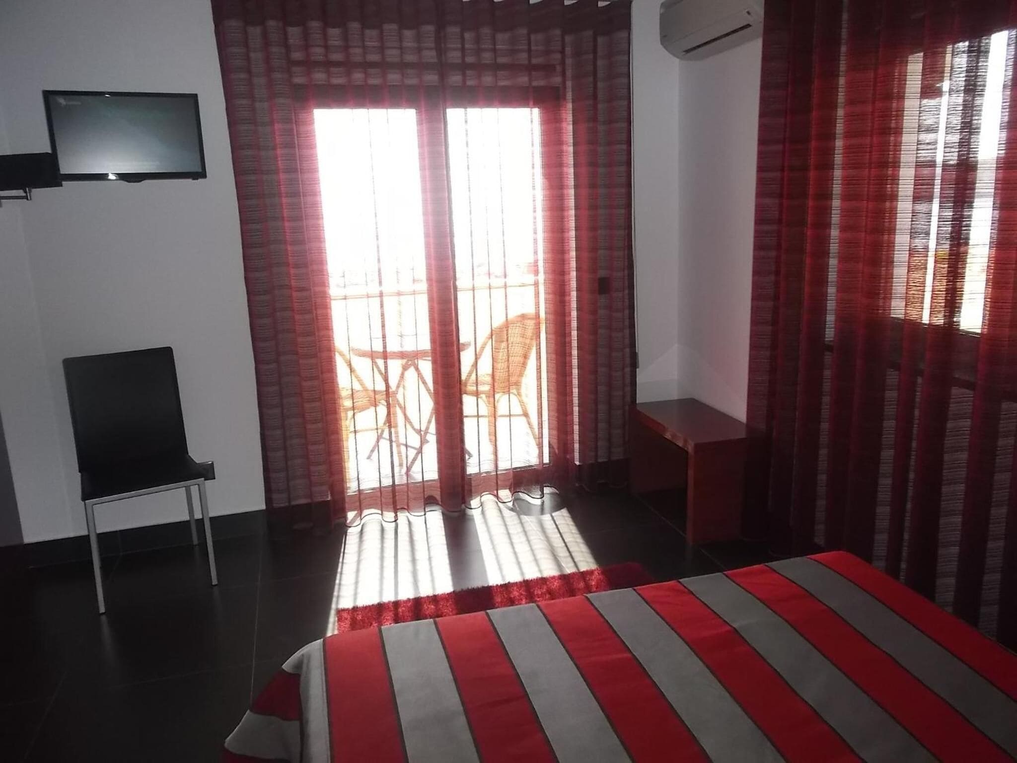 A hotel room with a bed, a chair, a TV, and a sliding door to a balcony.