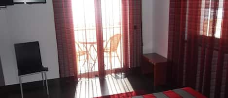 Habitación de hotel con cama, una silla, televisión y puerta corrediza a un balcón.