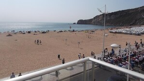 A beach with a clear view of the sea and cliffs. There are people walking and sitting on the sand.