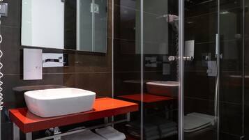 Un baño moderno con lavamanos blanco, encimera roja y cabina de ducha de vidrio.