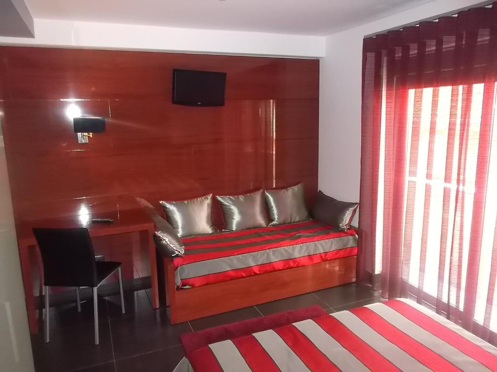 A bedroom with a bed, a desk, a chair, and a TV mounted on the wall.