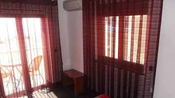 A room with a bed, a small table, and a chair. There is an air conditioning unit on the wall.