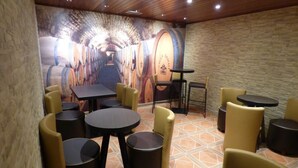 A restaurant with round tables and chairs, a stone floor, and a mural of wine barrels on the wall.