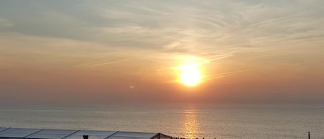 Un atardecer sobre una playa con cielo despejado, mar tranquilo y una estructura con techo en primer plano.