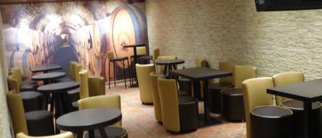 Restaurante com várias mesas e cadeiras, chão de azulejos e um mural na parede.