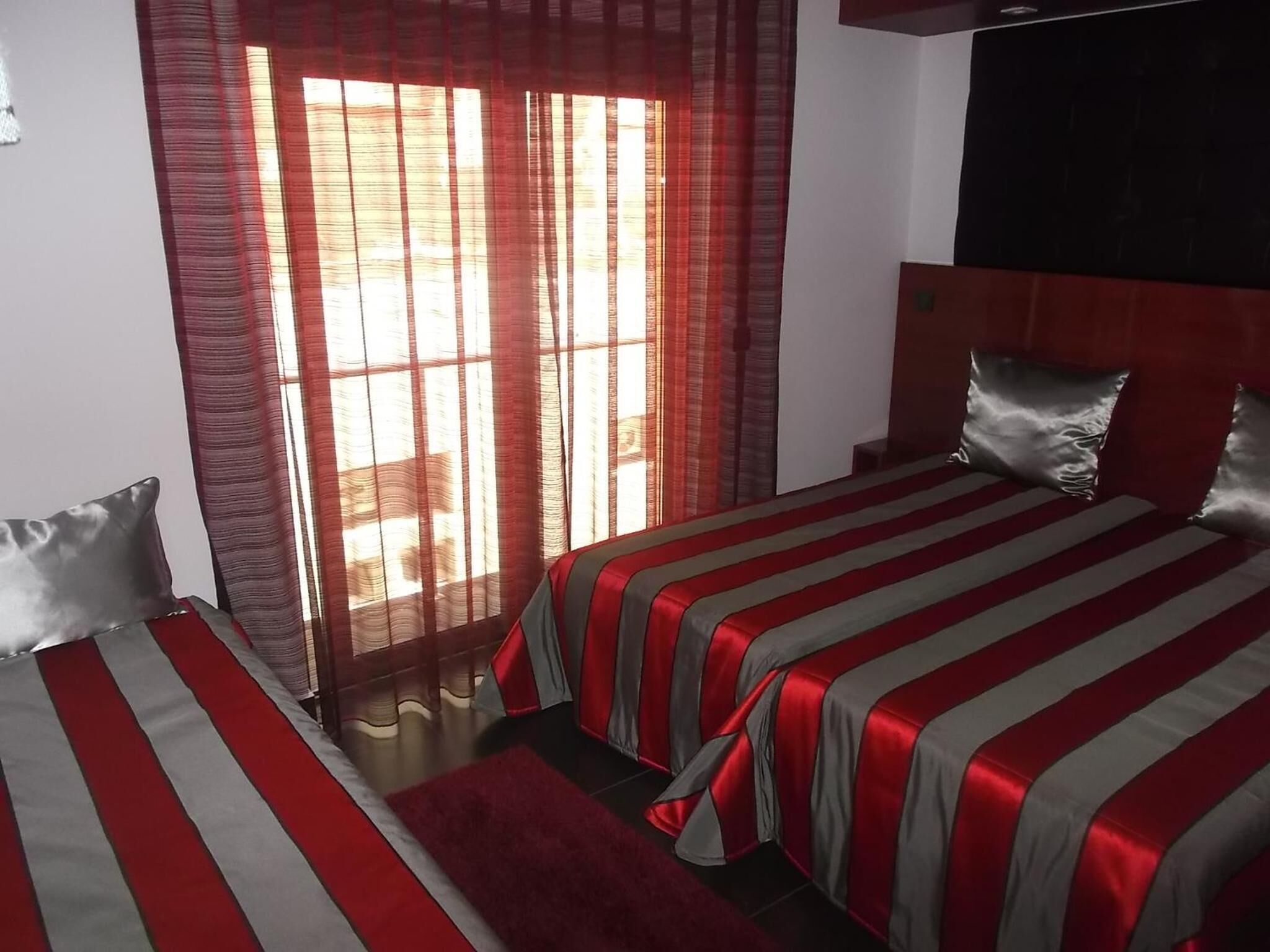 Hotellihuone, jossa on kaksi sänkyä, suuri ikkuna punaisilla verhoilla ja tumma pääty.