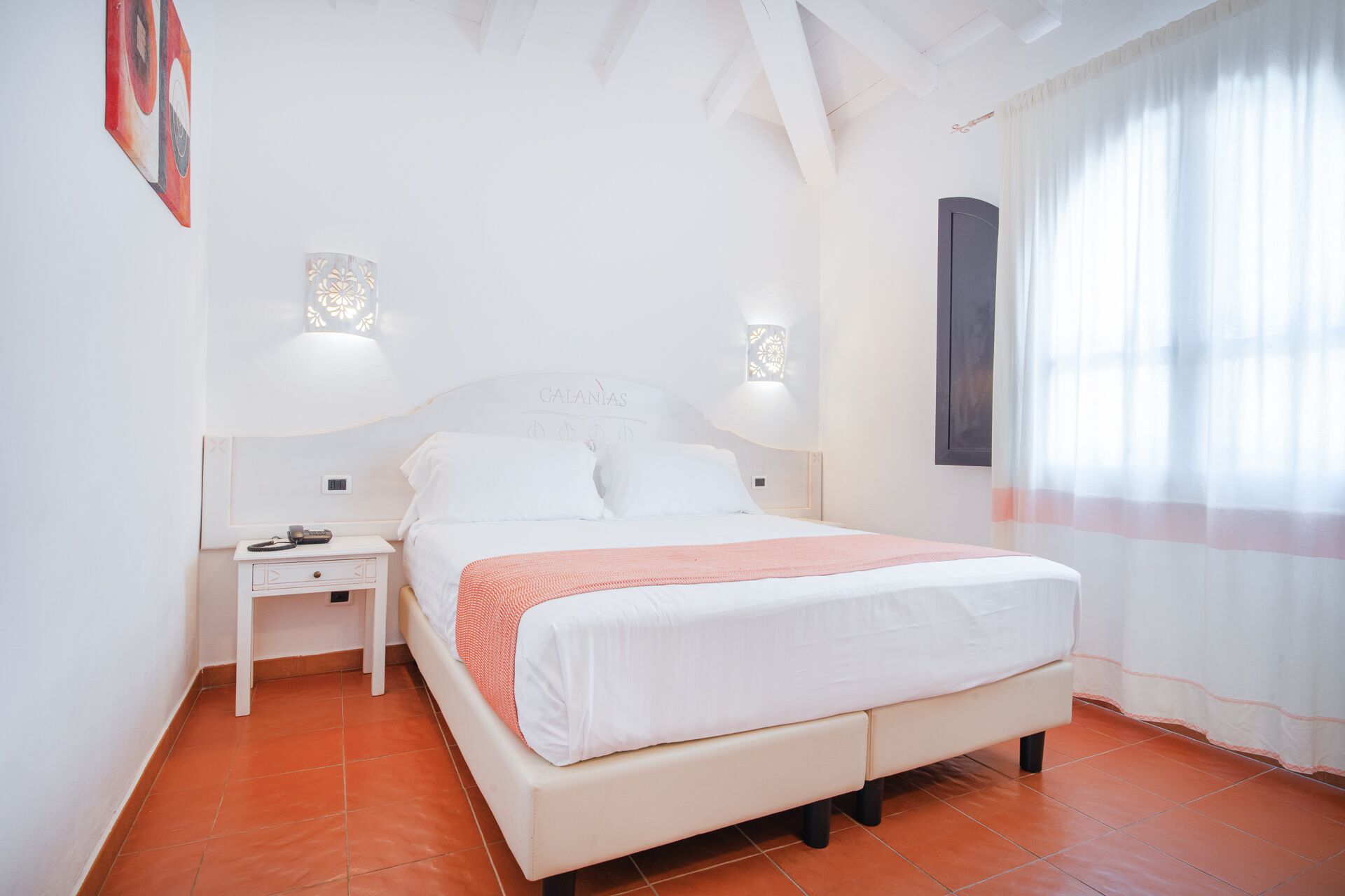 Una camera da letto con un letto, comodini, una lampada a parete e una finestra con tende.