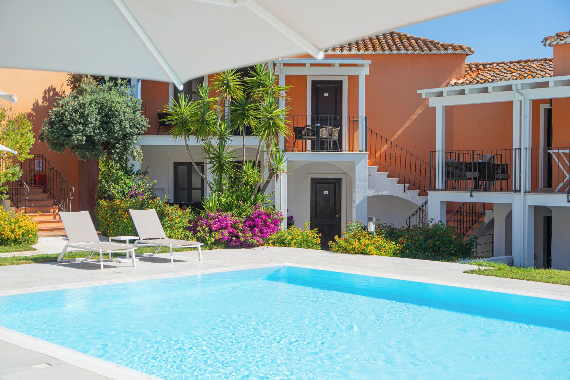 Una piscina con sillones de descanso, una escalera y un edificio con balcones.